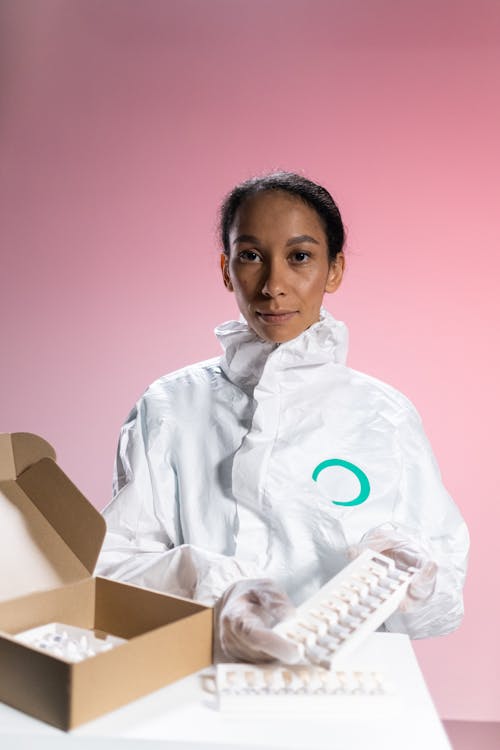 A Female Nurse Looking At Camera and Holding a Box of Vaccines in Plastic Gloves 