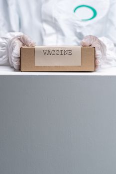 Healthcare worker in protective gear holding a vaccine package, emphasizing safety and health.