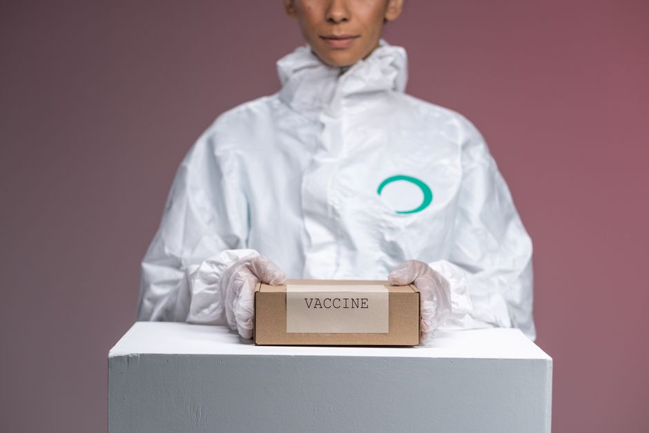 Medical worker in protective uniform holding a vaccine box in a studio setting.