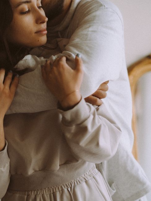 Intimate moment of a couple hugging warmly indoors, eyes closed.