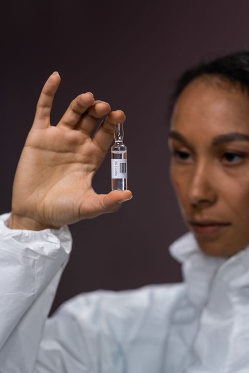 Free Focused scientist in protective gear examining a vaccine vial indoors. Stock Photo