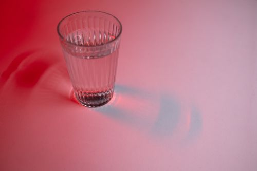 Free Close-up of a glass of water with a red lighting effect, casting dynamic shadows. Stock Photo