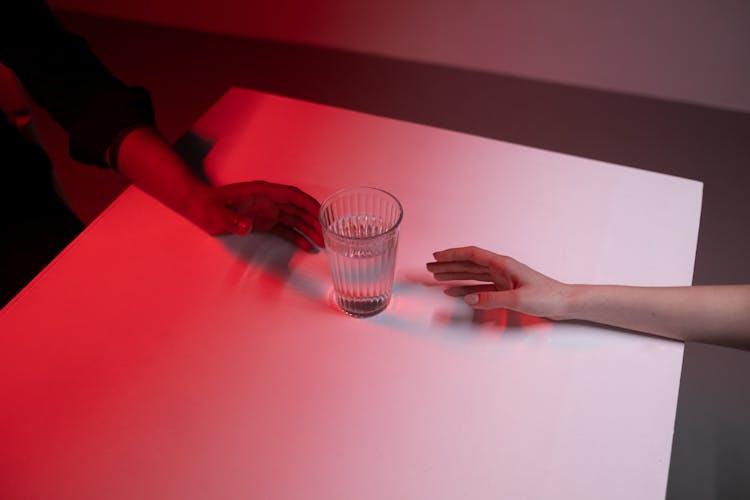 Two Peoples Hands Reaching Glass Of Water