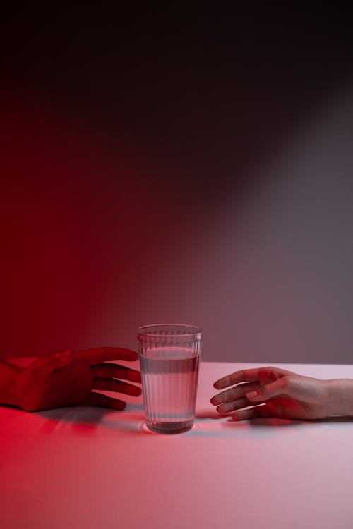 Two Peoples Hands by Glass of Water