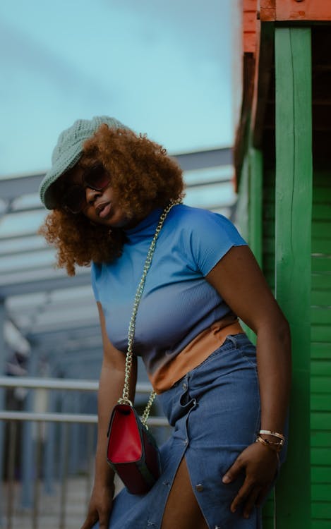 Woman in Blue Clothes Leaning on Green Buildings Beam