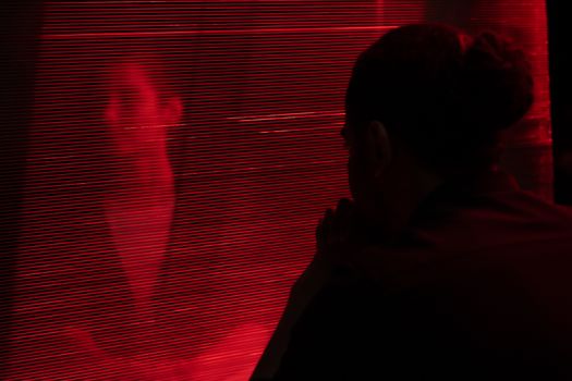 Silhouetted person behind a red translucent curtain creates a mysterious atmosphere.