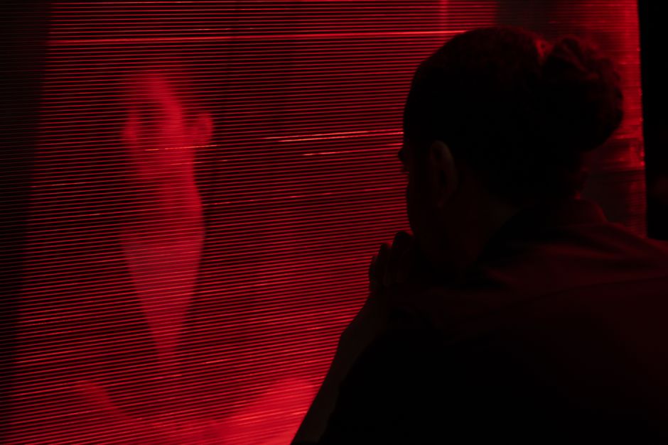 Silhouetted person behind a red translucent curtain creates a mysterious atmosphere.