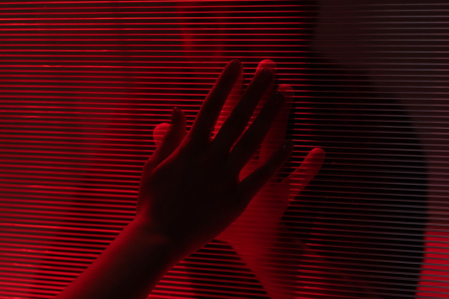 A hand pressed against red-lit textured glass — photo by Ron Lach on Pexels