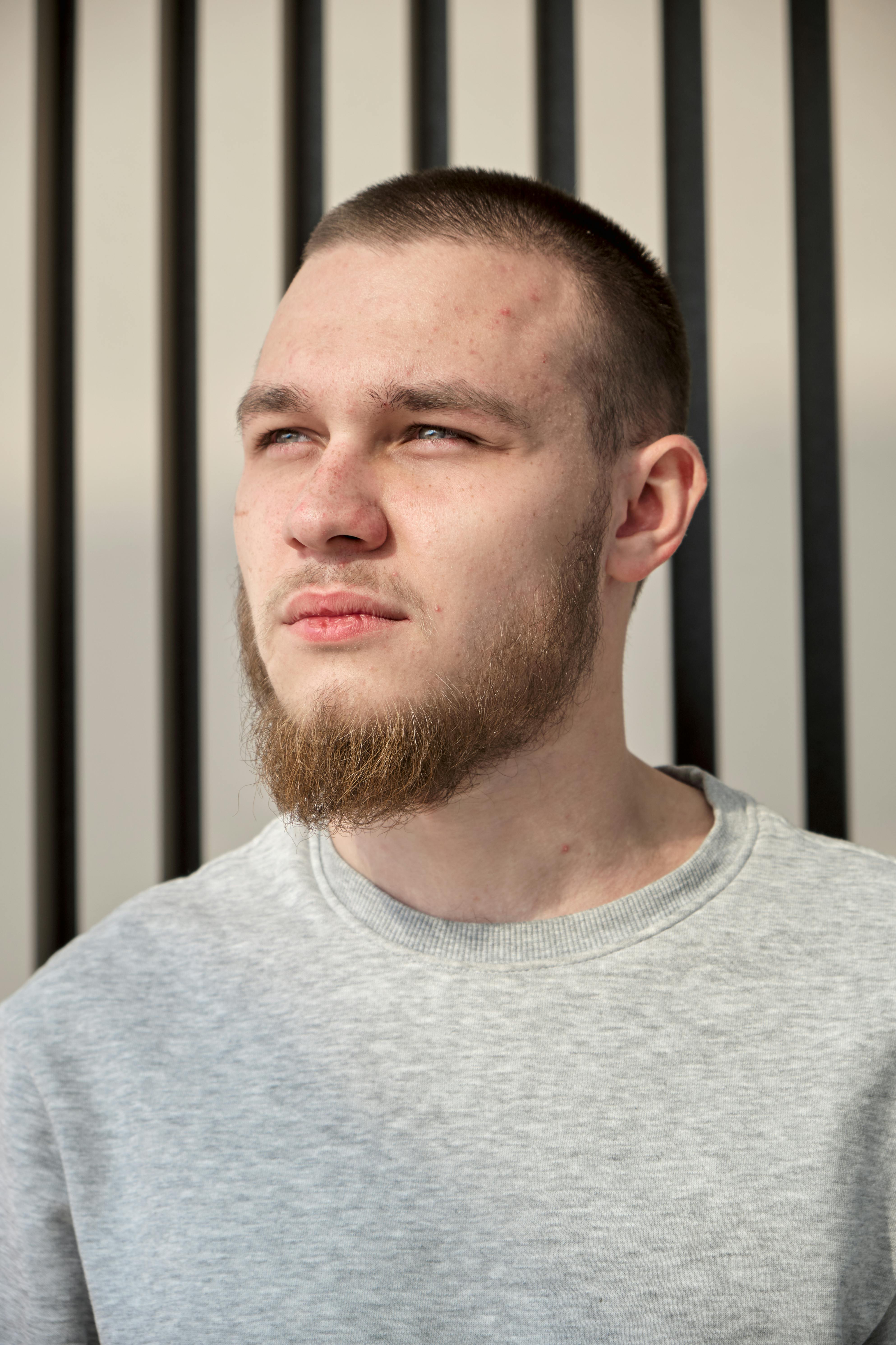 A young man with facial hair gazes thoughtfully, bathed in sunlight against a striped background.