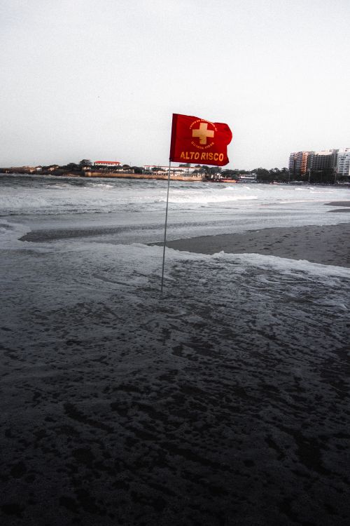 Free Red warning flag indicating high risk on a deserted beach with waves. Stock Photo