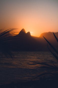 A stunning sunset view over the ocean with mountains silhouetted against a vibrant sky.