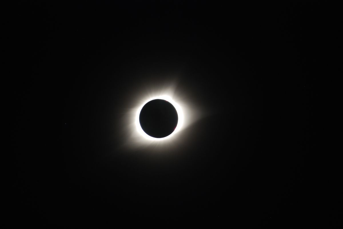 Total solar eclipse showing the sun's corona glowing around a darkened moon in the sky