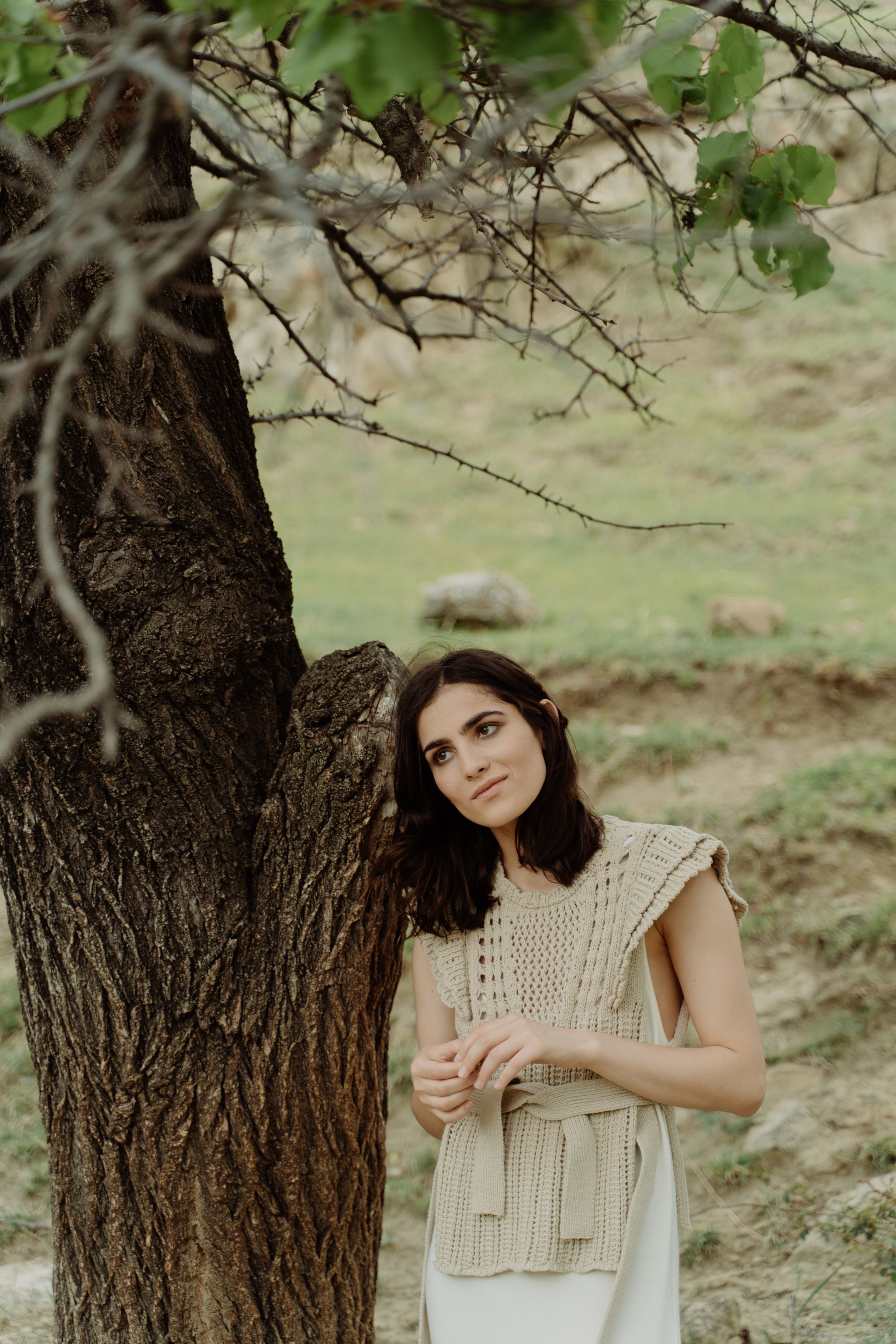 A serene scene of a woman standing by a tree in an outdoor setting, embracing nature.