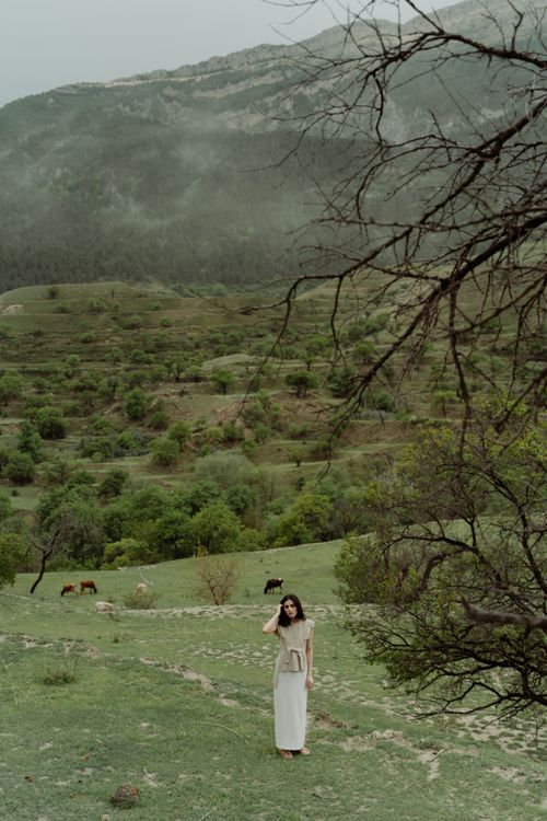 Free Woman standing in a lush, green mountain field surrounded by nature's tranquility. Stock Photo