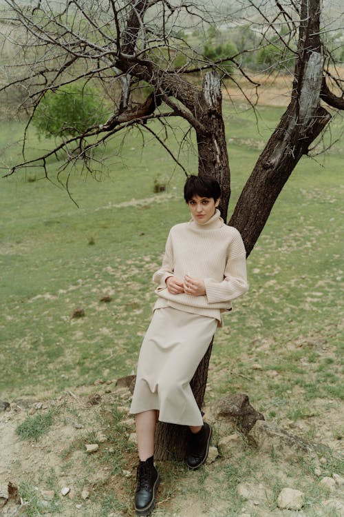 Photo of a Woman in a Beige Long Sleeve Shirt Leaning on a Tree