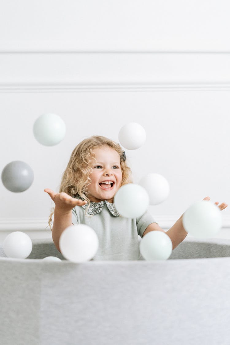 Child With Blond Hair Playing In A Pool With Balls