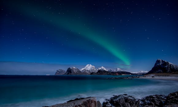 Captivating view of the Northern Lights illuminating snowy mountains in Nordland, Norway.