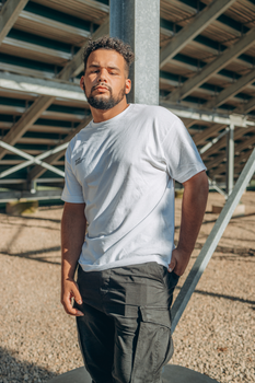 Casual photo of a man with a beard in a white t-shirt posing outdoors under a structure.
