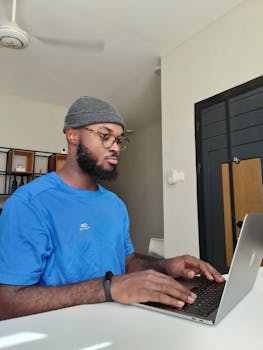 Focused man typing on a laptop indoors with natural daylight.