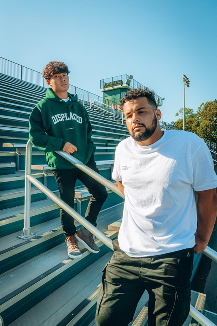 Fotomural Dos hombres con ropa casual posando en las gradas del estadio bajo la luz brillante del día.