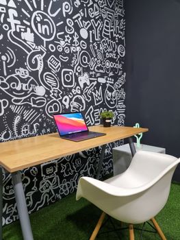 Contemporary office setup featuring a laptop on a wooden desk against a graffiti wall.