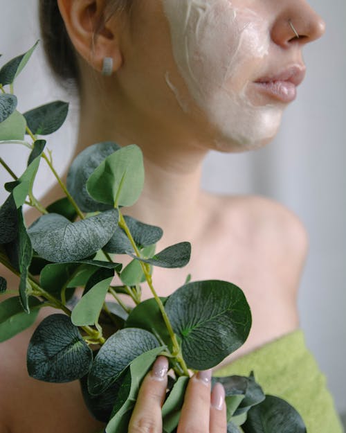 Close-Up View of Woman With Cream on Face Holding Leaves