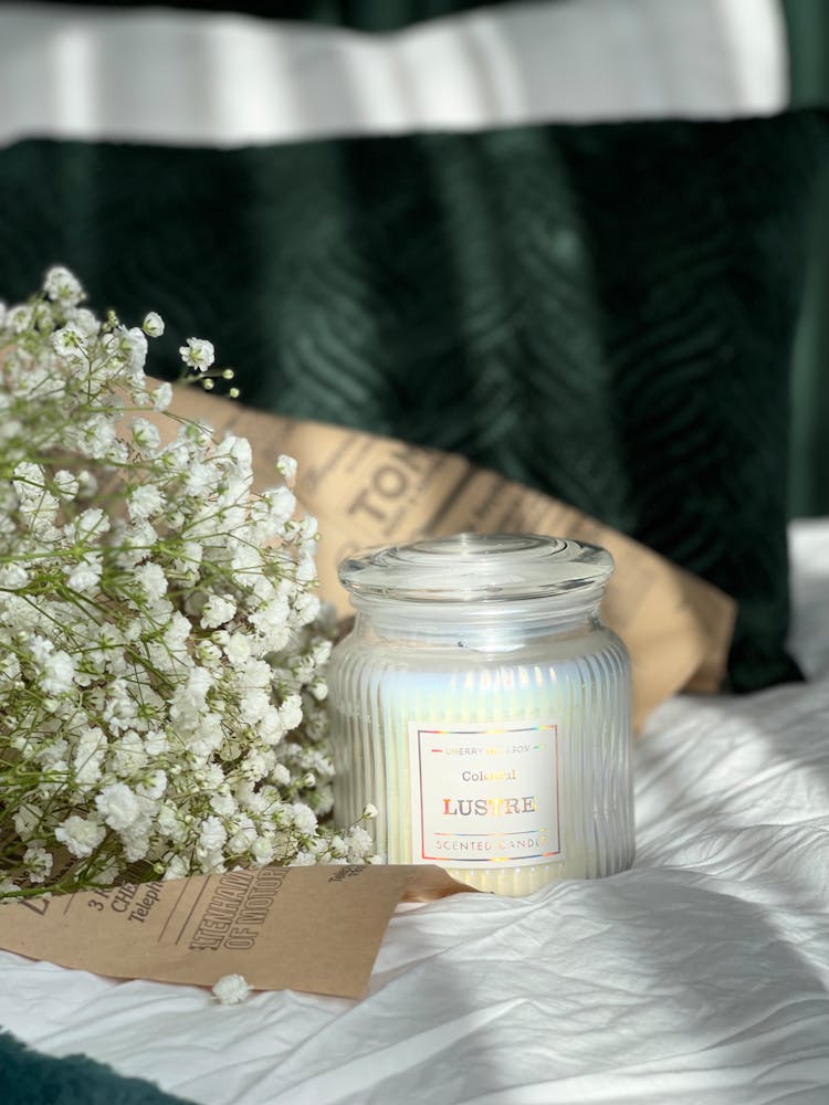 A Clear Jar Of Scented Candle Beside A Bouquet Of Baby's Breath Flowers