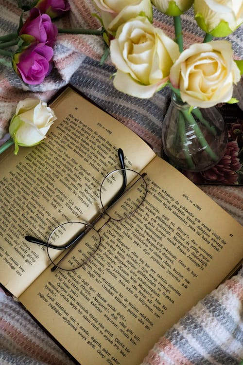 Free Glasses on Opened Book Next to Flowers in Glass  Stock Photo