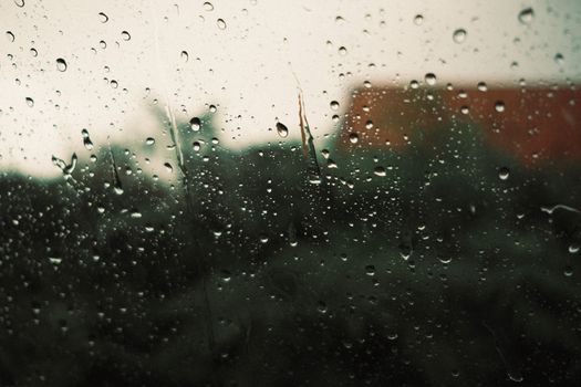 Close-up of raindrops on a window with a blurred backdrop, suggesting a rainy day.