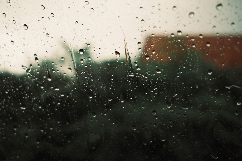 Close-up of raindrops on a window with a blurred backdrop, suggesting a rainy day.