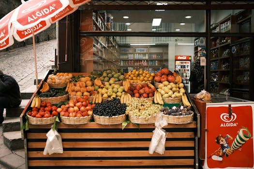 Vibrant display of assorted fruits at an outdoor market stand with baskets of bananas, grapes, and more.