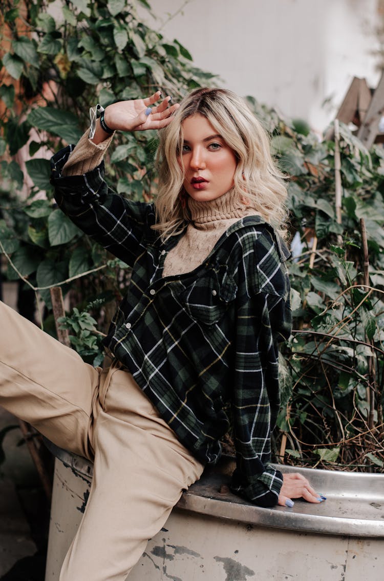 Blond Young Woman Leaning Against Large Plant Pot And Posing