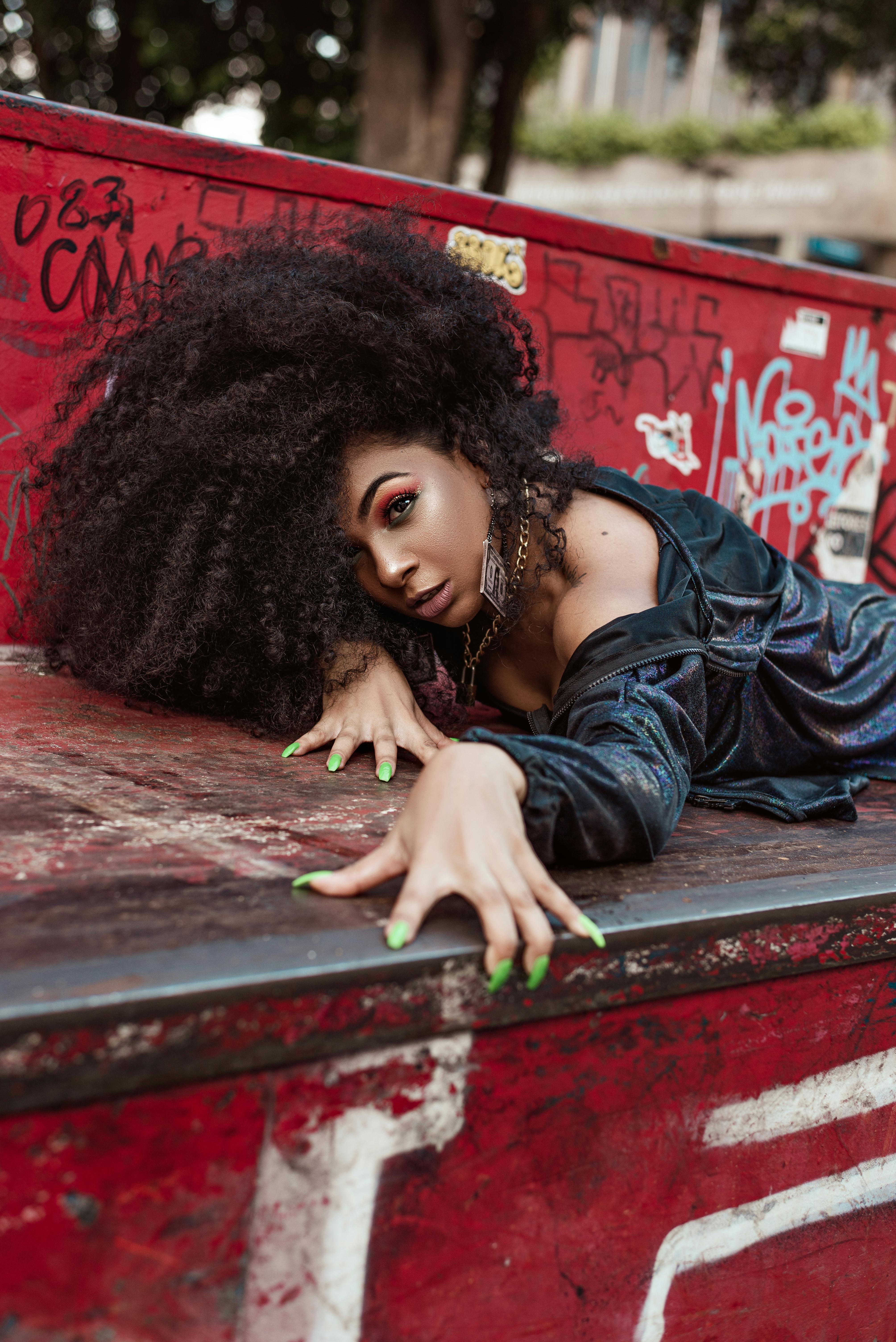 beautiful woman with long curly hair laying on garbage container