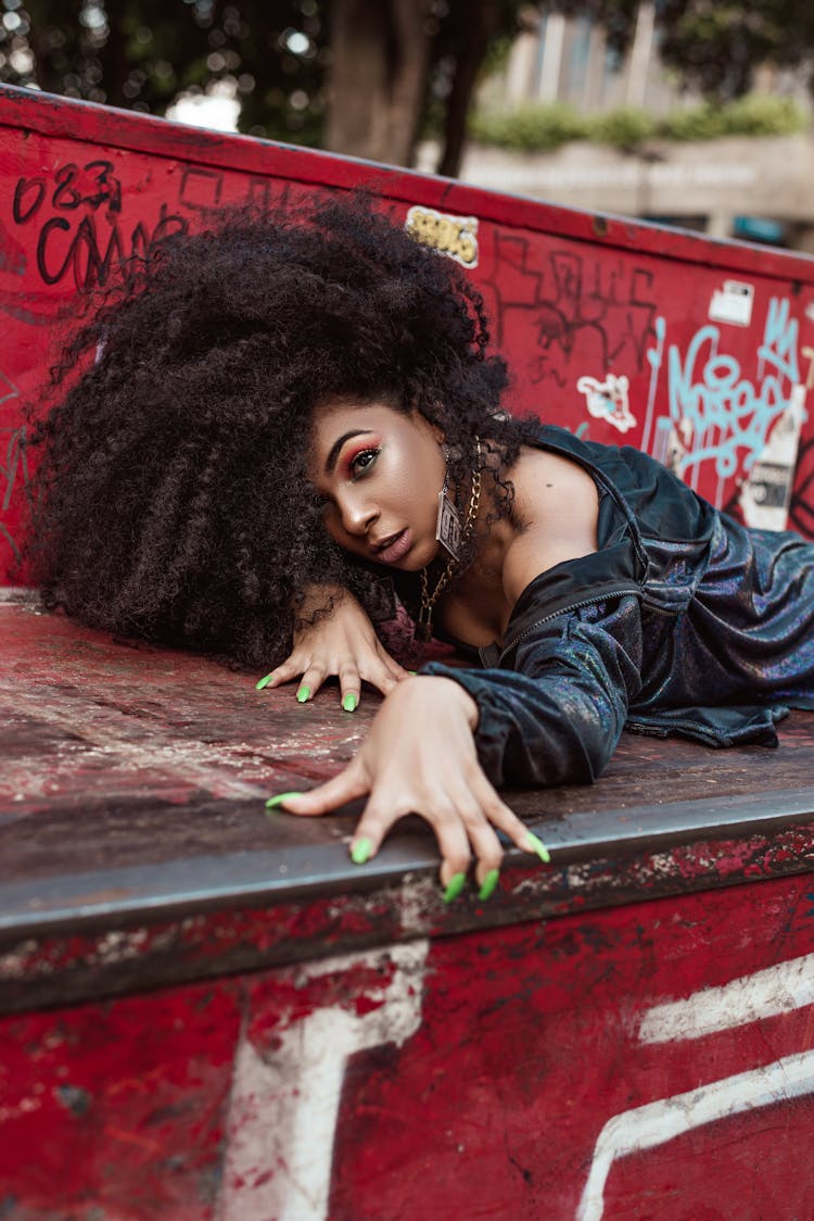 Beautiful Woman With Long Curly Hair Laying On Garbage Container