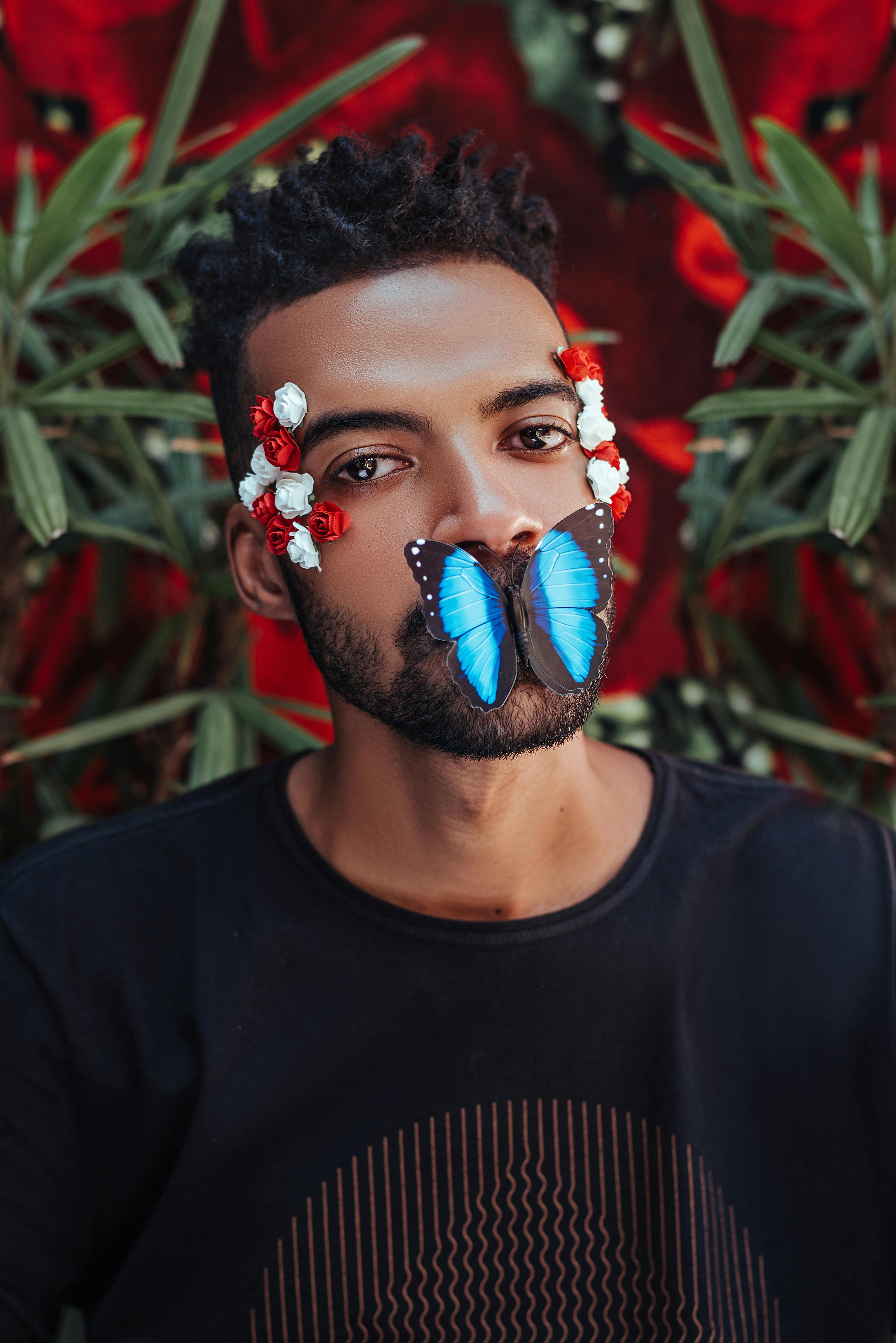 man with exotic butterfly on his mouth and flowers on his temples