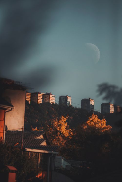 Free Scenic view of concrete buildings on hill with half moon and autumn trees. Stock Photo