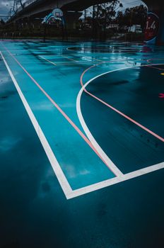 Vibrant basketball court with wet reflections after rain, showcasing a moody sports setting.