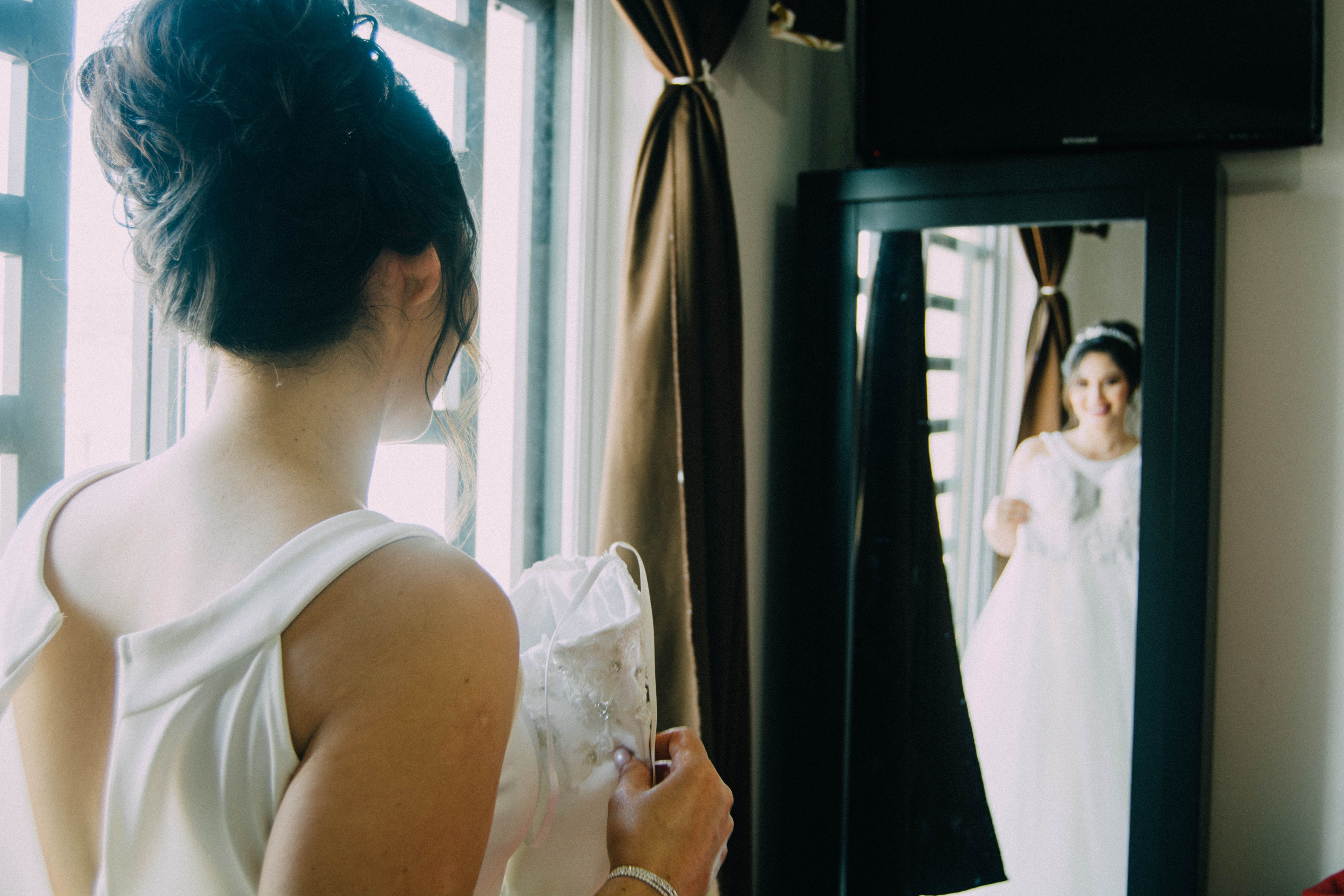 A bride looking at her reflection in a mirror, wearing an elegant bridal gown and a stylish hair bun.