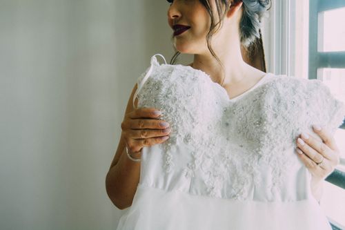 Free A bride holding her detailed wedding dress, ready for her special day. Soft natural light adds elegance. Stock Photo