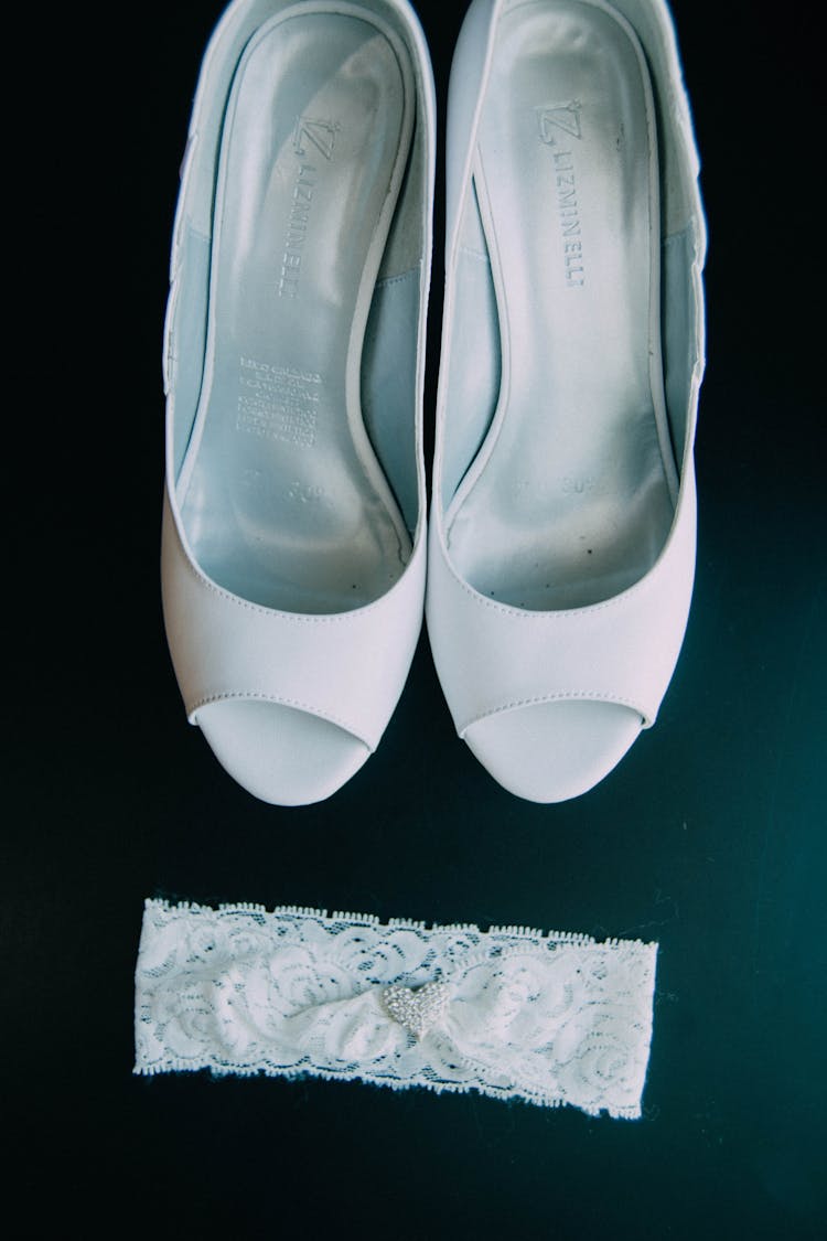 A White Bridal Shoes Beside A Wedding Garter