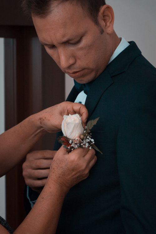 Free A groom prepares by having a white rose boutonniere pinned to his suit. Stock Photo