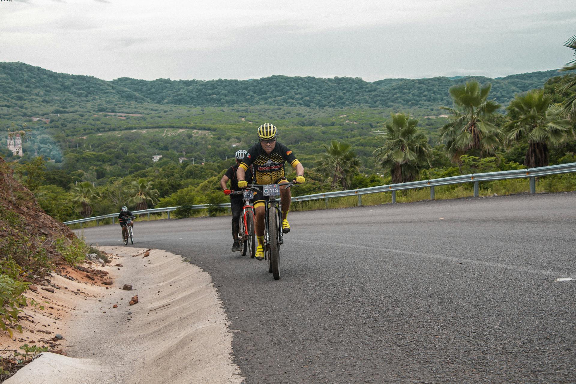 Group of cyclists racing uphill on a scenic mountain road surrounded by lush greenery.