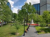 A sunny day at a lush urban park in downtown Montreal with people relaxing among green trees and high-rise buildings.