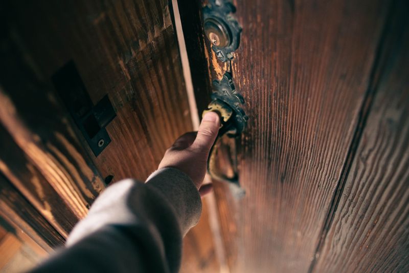 Close-up view of a hand opening a vintage wooden door with ornate handle, creating a warm and inviting atmosphere.