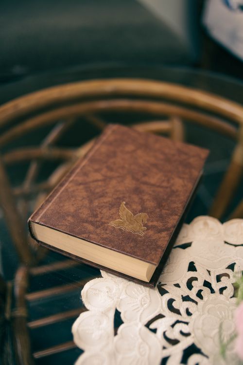Free A vintage book with embossed pegasus cover resting on a round glass table with lace decor. Stock Photo