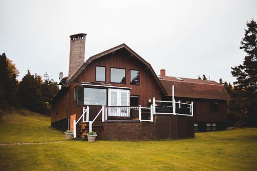 Free Beautiful wooden house with a chimney surrounded by lush forest and green grass, offering tranquility. Stock Photo