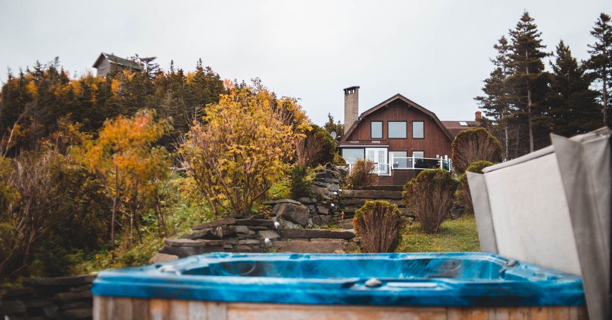 A serene countryside house surrounded by autumn foliage with a hot tub in the foreground.