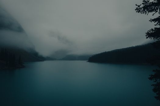 A foggy view of Moraine Lake surrounded by dense forest in Banff National Park, Canada.