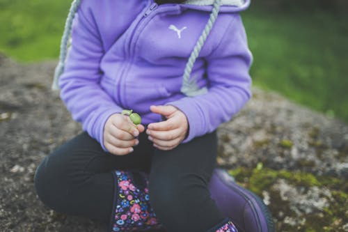 Child Wearing Purple Jacket Sitting on a Rock