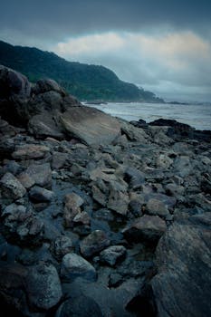 Rugged rocky seashore with waves crashing under a cloudy sky, creating a dramatic coastal scene.